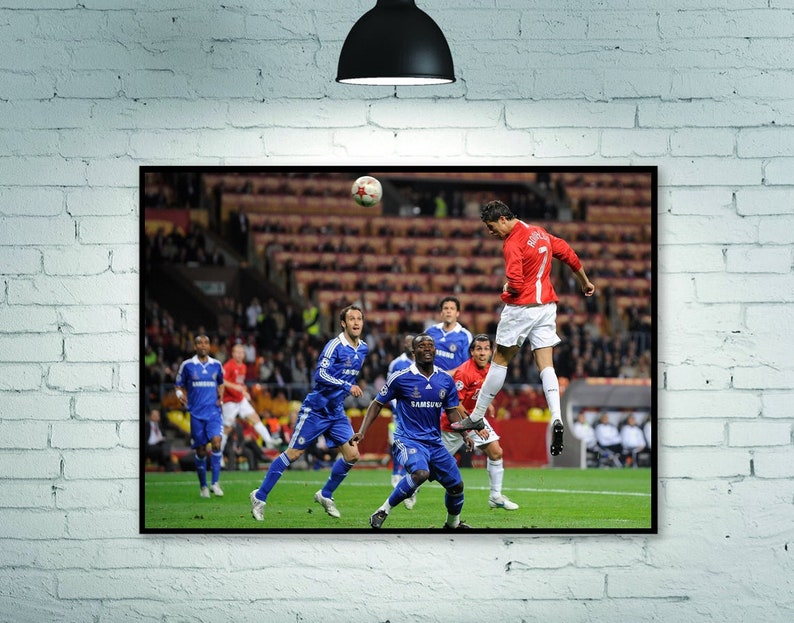 May include: A soccer player in a red jersey jumps in the air to head the ball.  Other players in blue jerseys are on the field.  The game is being played in a stadium with a large crowd.