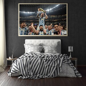 May include: Framed photograph of a soccer player holding a trophy, surrounded by teammates in a stadium. The player is wearing a blue and white striped jersey. The photograph is displayed above a bed with a striped blanket.