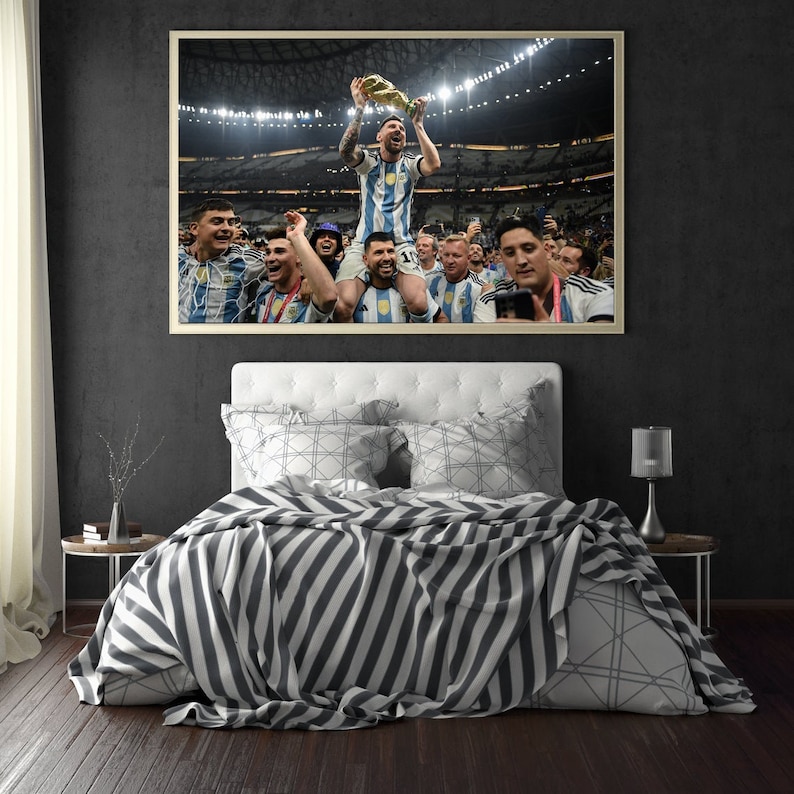 May include: Framed photograph of a soccer player holding a trophy, surrounded by teammates in a stadium. The player is wearing a blue and white striped jersey. The photograph is displayed above a bed with a striped blanket.