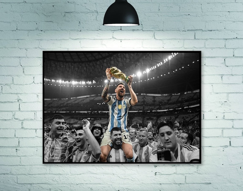 May include: A framed black and white photograph of a soccer player holding a trophy above his head, surrounded by cheering teammates. The player is wearing a light blue and white striped jersey. The image is set against a black background.