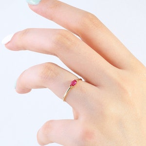 Pode incluir: Um anel de ouro com uma única gema vermelha. O anel está no dedo de uma pessoa.