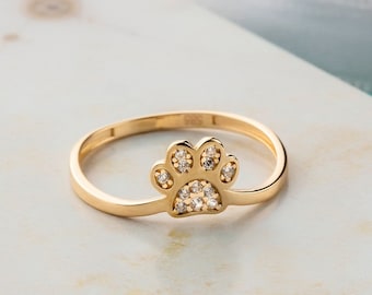 Puede incluir: Un anillo de oro con un diseño de huella de pata adornado con pequeñas piedras transparentes.