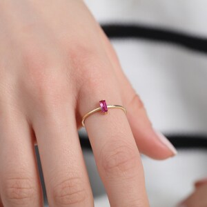 May include: A delicate gold ring with a single pink rectangular gemstone.