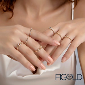 May include: A set of six gold rings with clear and blue gemstones. The rings are stacked on a person's fingers. The rings are delicate and sparkly. The image includes the text "FIGOLD".