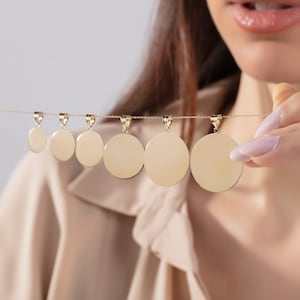 May include: A set of five gold-toned round pendant charms of varying sizes hanging on a chain. The charms are blank and smooth.