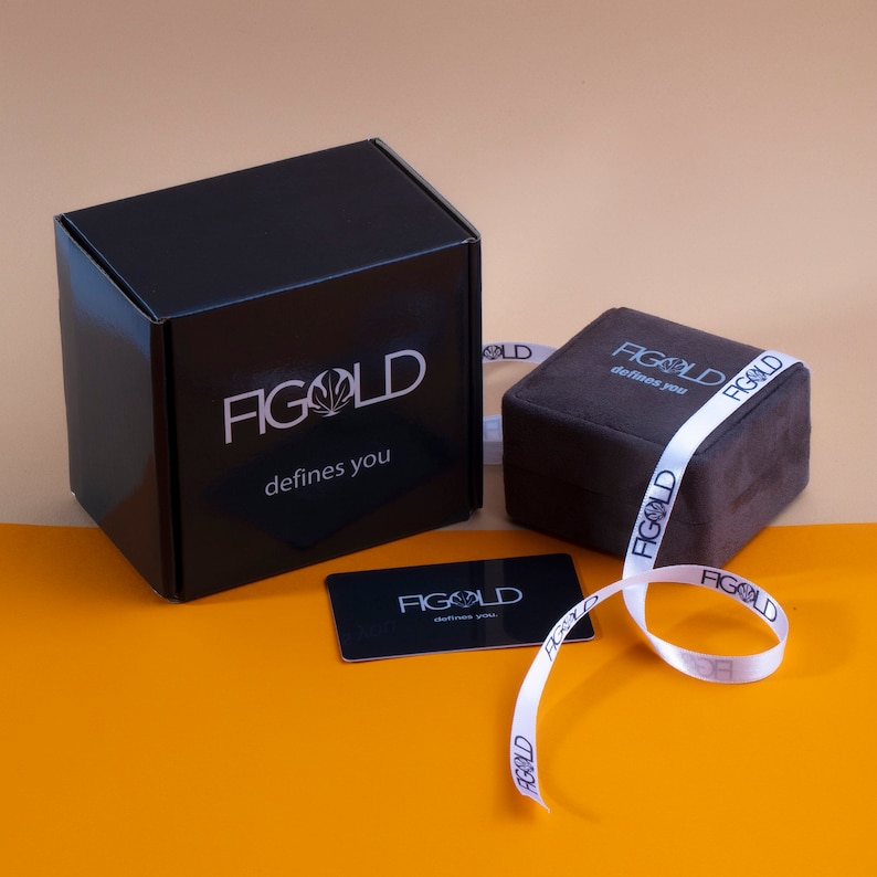 May include: A black box with the text "FIGOLD defines you" on it. A smaller brown box with the same text is next to it. A white ribbon with the same text is wrapped around the boxes.