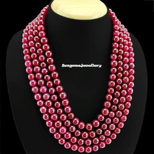 May include: A multi-strand necklace made of deep red gemstone beads. The necklace is made of four strands of round beads, each strand is approximately 46 cm long. The beads are a deep red colour and have a smooth, polished finish. The necklace is a beautiful and elegant piece of jewellery.