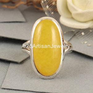 May include: A silver ring with a large oval yellow gemstone. The ring is set in a silver band with a smooth finish.