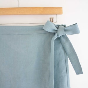 Pu&ograve; includere: Una gonna avvolgente blu chiaro con una cintura da annodare. La gonna &egrave; realizzata in tessuto di lino e ha un design semplice ed elegante.