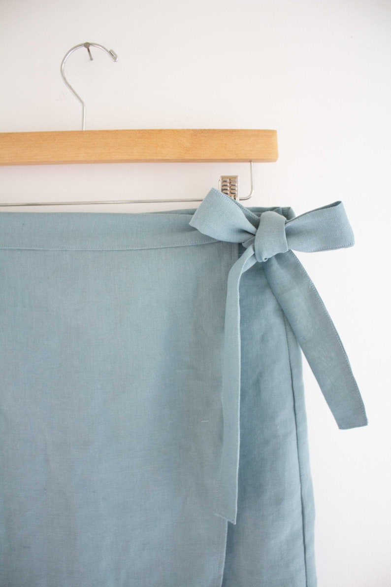 Pu&ograve; includere: Una gonna avvolgente blu chiaro con una cintura da annodare. La gonna &egrave; realizzata in tessuto di lino e ha un design semplice ed elegante.