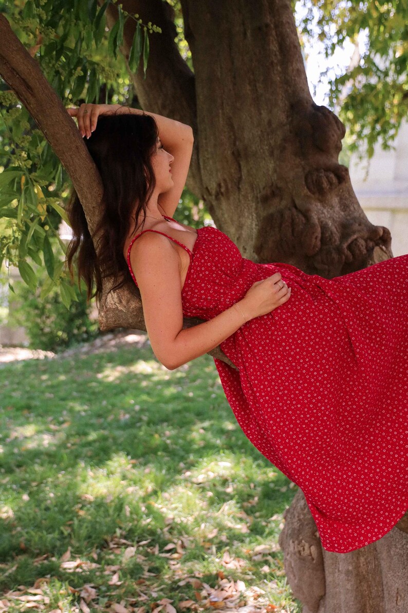 May include: A sleeveless red midi dress featuring a small white floral pattern, a straight neckline, and thin shoulder straps. The garment is constructed with a fitted bodice that transitions into a flowing skirt, showcasing a consistent print.