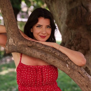 May include: A bright red sleeveless dress featuring a small white floral pattern, a gathered square neckline, and a smocked bodice. The garment has thin shoulder straps and a flared skirt, providing a simple and consistent design throughout the piece.