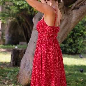 May include: A vibrant red midi dress featuring a delicate white floral pattern, thin spaghetti straps, a fitted bodice with a gathered waistline, and a flowing skirt that falls below the knees, showcasing a simple and classic silhouette.
