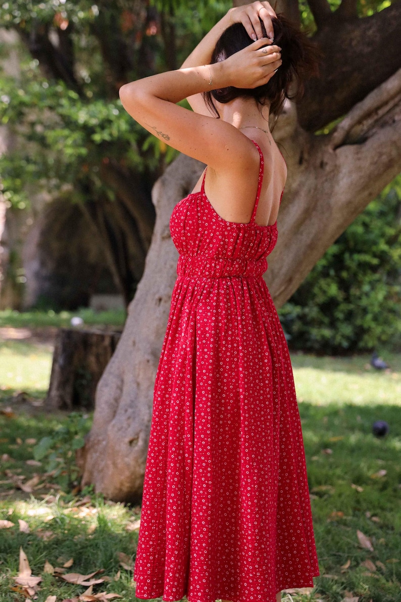 May include: A vibrant red midi dress featuring a delicate white floral pattern, thin spaghetti straps, a fitted bodice with a gathered waistline, and a flowing skirt that falls below the knees, showcasing a simple and classic silhouette.