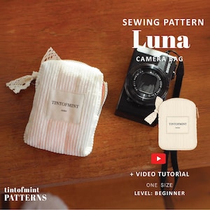 May include: A white corduroy camera bag sewing pattern titled Luna by TINTOFMINT. The pattern includes a small white corduroy pouch with a lace zipper pull, a black Canon camera, and a smaller pouch graphic. Text includes SEWING PATTERN Luna CAMERA BAG, TINTOFMINT, + VIDEO TUTORIAL, ONE SIZE, LEVEL: BEGINNER.