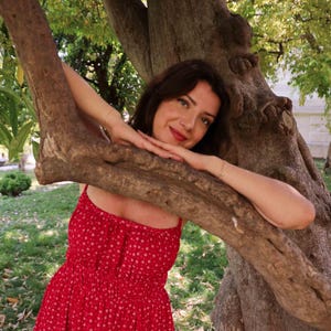May include: A bright red sleeveless dress featuring a small white floral pattern, a square neckline, and a gathered, elasticised bodice that transitions into a flowing skirt. The garment is constructed with thin shoulder straps and a simple silhouette.