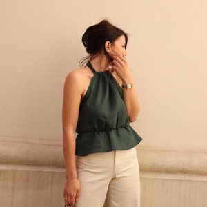 Peut inclure: Une femme portant un haut halter vert fonc&eacute; avec un volant blanc et un pantalon blanc &agrave; jambes larges. Elle tient un sac fourre-tout en osier brun.