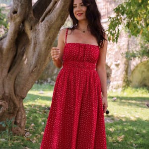 May include: A midi-length red dress featuring a small white floral pattern, a square neckline, thin shoulder straps, and a gathered elasticated waistline that flows into a full skirt. The garment is constructed with a fitted bodice and a flared hem.