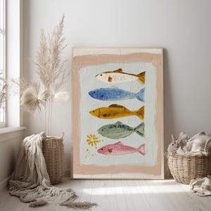 May include: A framed art print depicting five fish in various colours: brown, blue, gold, green, and pink. The fish are painted on a light blue background with a textured, off-white border. The artwork has a rustic, hand-painted appearance.