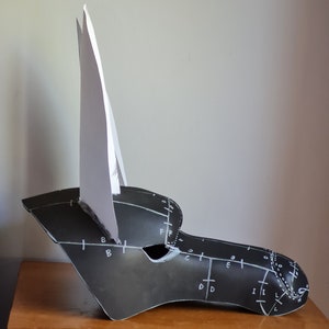 May include: A black and white paper mask with a white paper ear on the left side. The mask has markings on it, including letters and numbers.