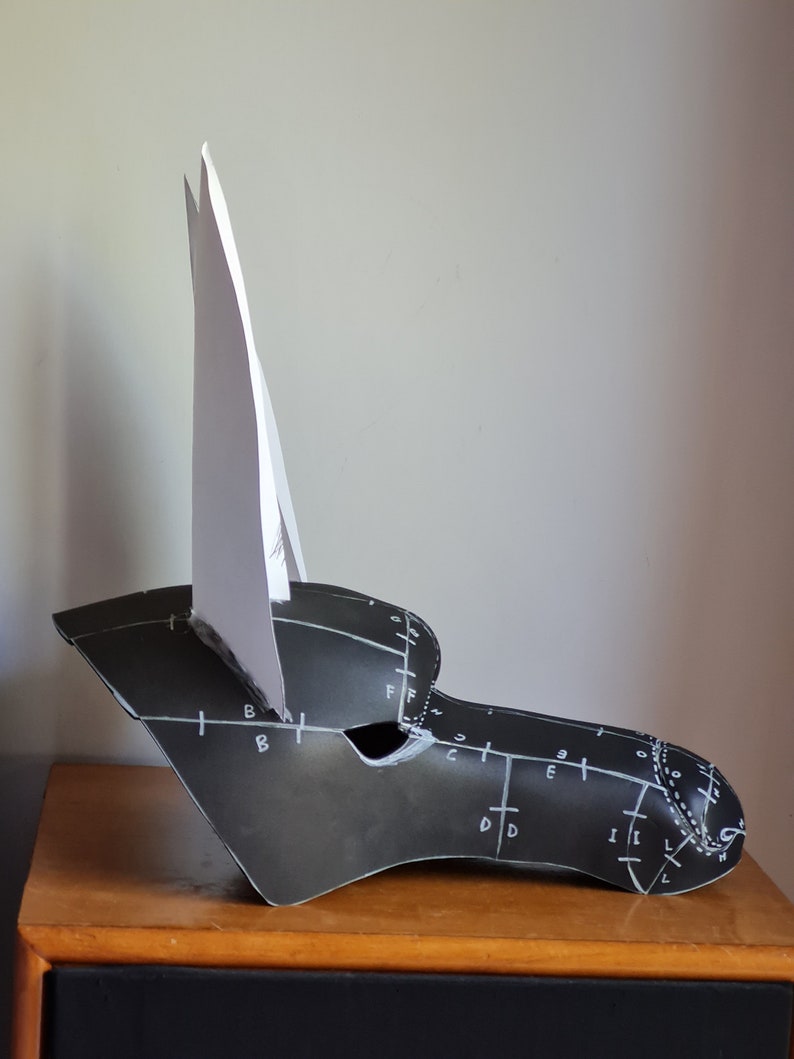 May include: A black and white paper mask with a white paper ear on the left side. The mask has markings on it, including letters and numbers.