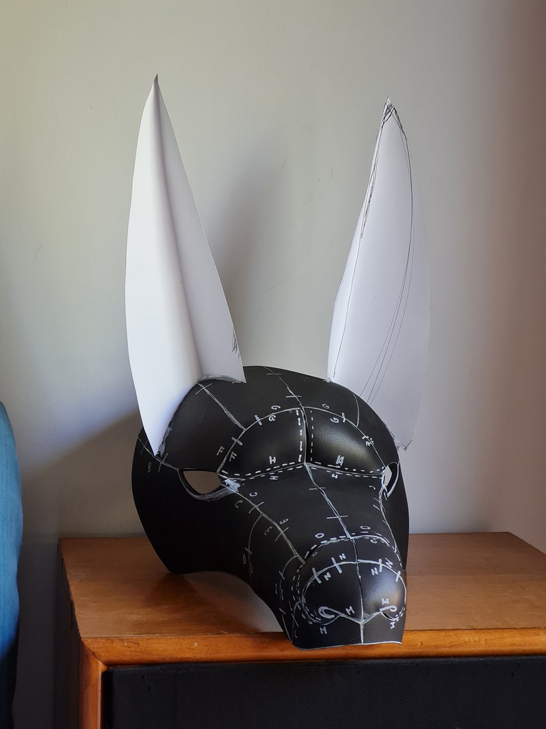May include: A black and white mask with a pattern of lines and circles. The mask has two large white ears.