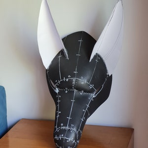 May include: A black foam mask with white paper ears. The mask has a grid pattern drawn on it with letters and numbers.
