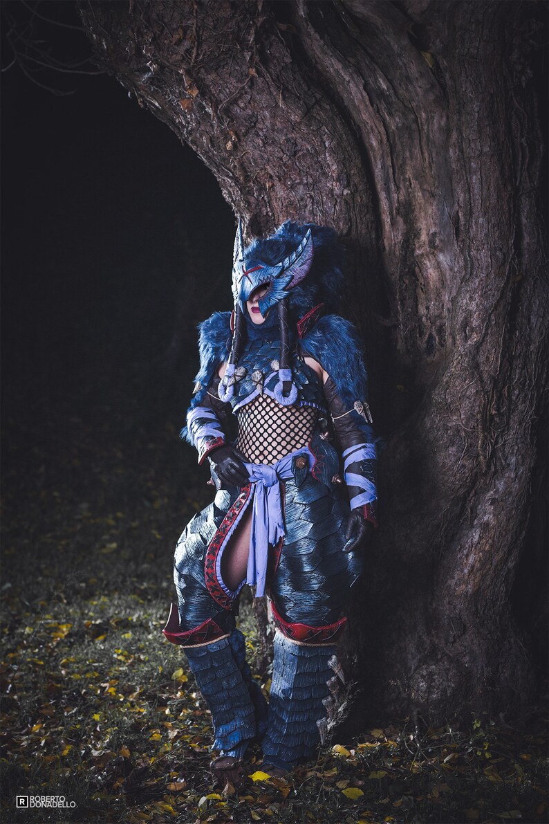 Puede incluir: Una persona vestida con un traje azul y rojo con una m&aacute;scara de lobo. El traje est&aacute; decorado con piel, escamas y armadura. La persona est&aacute; de pie frente a un &aacute;rbol.