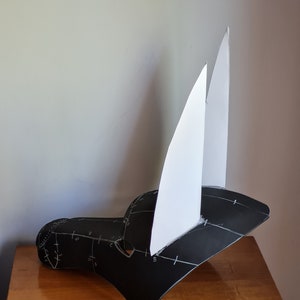 May include: A black paper mask with white paper ears. The mask has markings on it, possibly for cutting and assembly.