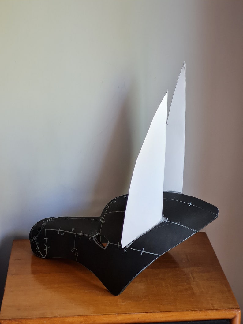 May include: A black paper mask with white paper ears. The mask has markings on it, possibly for cutting and assembly.