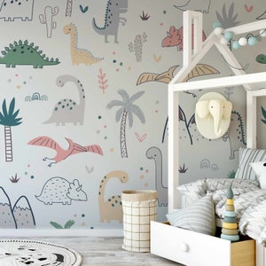 May include: A light gray nursery wall mural with a dinosaur theme. The mural features various dinosaurs, including a green stegosaurus, a pink pterodactyl, and a yellow brachiosaurus. There are also palm trees, cacti, and other plants on the mural.