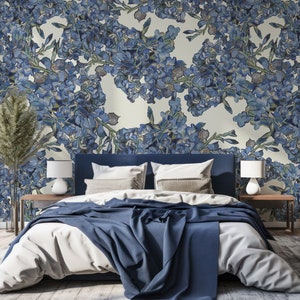 May include: A blue and white floral patterned wallpaper with a blue headboard bed with white bedding and a blue throw blanket. Two bedside tables with lamps are on either side of the bed.