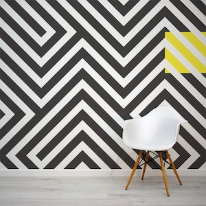 Puede incluir: Una silla blanca con patas de madera delante de una pared con patrón geométrico en blanco y negro con un acento de franja amarilla.