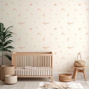Puede incluir: Una habitación de bebé con una pared blanca con un papel tapiz de color melocotón con un patrón repetido de criaturas marinas. Una cuna de madera con un colchón blanco está en primer plano. Una cesta de mimbre y una pequeña mesa de madera con una cesta de mimbre en la parte superior también están en la habitación.