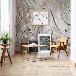 May include: A living room interior with a wood-grain patterned wallpaper, a yellow armchair, a wooden coffee table, a wooden stool, a lamp, and two framed prints with geometric shapes.
