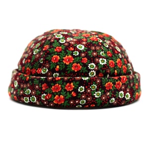 May include: A corduroy beanie hat with a floral pattern. The hat features a dark brown base with a repeating pattern of red, orange, and white flowers and green leaves. The brim is a darker shade of brown.