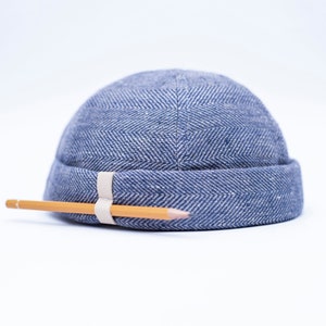 May include: A blue herringbone patterned skull cap with a light-colored band and a pencil. The cap is made of a textured fabric. The pencil is yellow with a gray eraser.