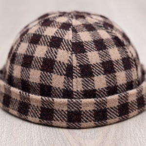May include: A brown and tan plaid beanie hat. The hat is made of a soft, woven fabric and features a classic, rolled-up brim. The plaid pattern is a repeating square design. The hat is a stylish accessory for cold weather.