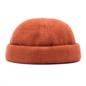 May include: A burnt orange beanie hat with a rolled brim. The hat is made of a textured fabric and sits on a white background. The hat is a classic style, suitable for various casual outfits.