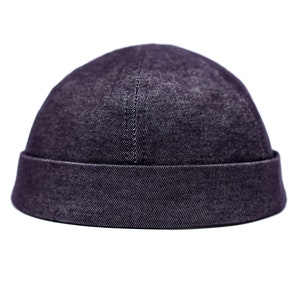 May include: A dark indigo denim cap with a folded brim. The cap has a rounded crown and a vertical seam. The fabric has a textured appearance. This hat is a stylish accessory.