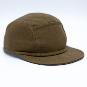 Peut inclure: Casquette en toile vert olive avec une petite visière. La casquette présente un design structuré à cinq panneaux. Le tissu semble être une toile durable et finement tissée. La casquette est de couleur unie, sans marque ni ornement visible.