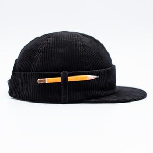 May include: Black corduroy hat with a flat peak, with a pencil inserted through a fabric loop. The pencil is yellow with a brown eraser and a sharpened graphite tip. The hat has a structured, rounded crown.