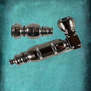 May include: Two silver metal smoking pipes. One pipe is a straight tube with a rounded end. The other pipe is a curved pipe with a bowl on top.