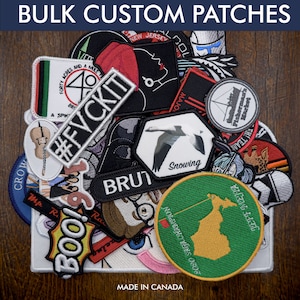 May include: A collection of custom embroidered patches in various colours, shapes, and designs. The patches feature different text, images, and logos, including "#FVCKIT", "BRUT", "Snowing", and "JEFF MEJIA". The patches are arranged on a wooden surface with the text "MADE IN CANADA" visible at the bottom.