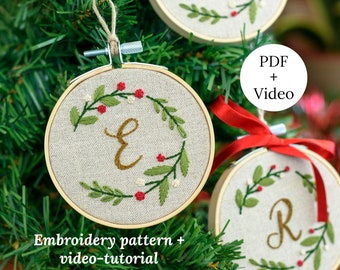 Pode incluir: Três enfeites de Natal bordados com as letras E, P e R em fio dourado, cercados por folhas verdes e bagas vermelhas. Os enfeites estão em uma árvore de Natal verde. O texto "PDF + Vídeo" e "Padrão de bordado + vídeo-tutorial" também está visível.