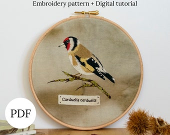 May include: Embroidered pattern of a goldfinch bird on a branch, with the text "Carduelis carduelis" on a beige fabric background. The embroidery is in a wooden hoop.