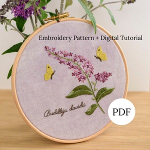 May include: Embroidered hoop art featuring a purple Buddleja davidii flower with two yellow butterflies, on a light purple fabric background. The text "Buddleja davidii" and "PDF" are also embroidered on the fabric.