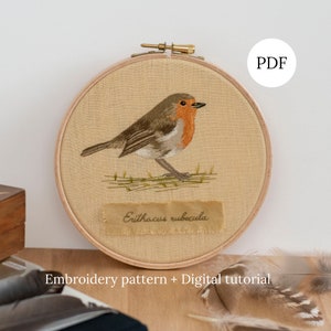 May include: Embroidered pattern of a robin, with the scientific name "Erithacus rubecula" written on a label below the bird. The embroidery is displayed in a wooden hoop, with a PDF label in the top right corner. The text "Embroidery pattern + Digital tutorial" is written below the hoop.