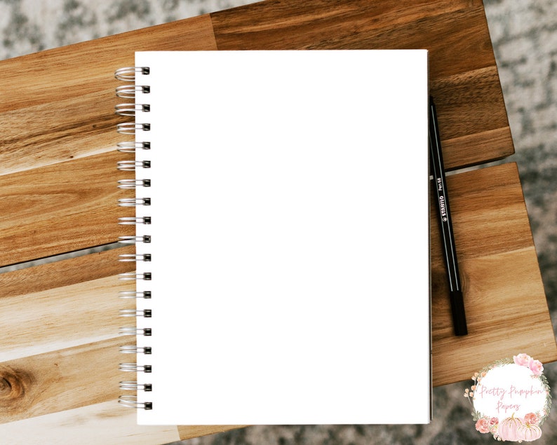 Pode incluir: Um caderno branco com espiral e uma caneta preta sobre uma superf&iacute;cie de madeira. O caderno est&aacute; em branco e pronto para ser escrito.