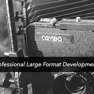 May include: Black and white image of a large format camera, with the brand name CAMBO visible. The camera has a bellows design and various adjustment knobs and scales. The text "Professional Large Format Development" is displayed.